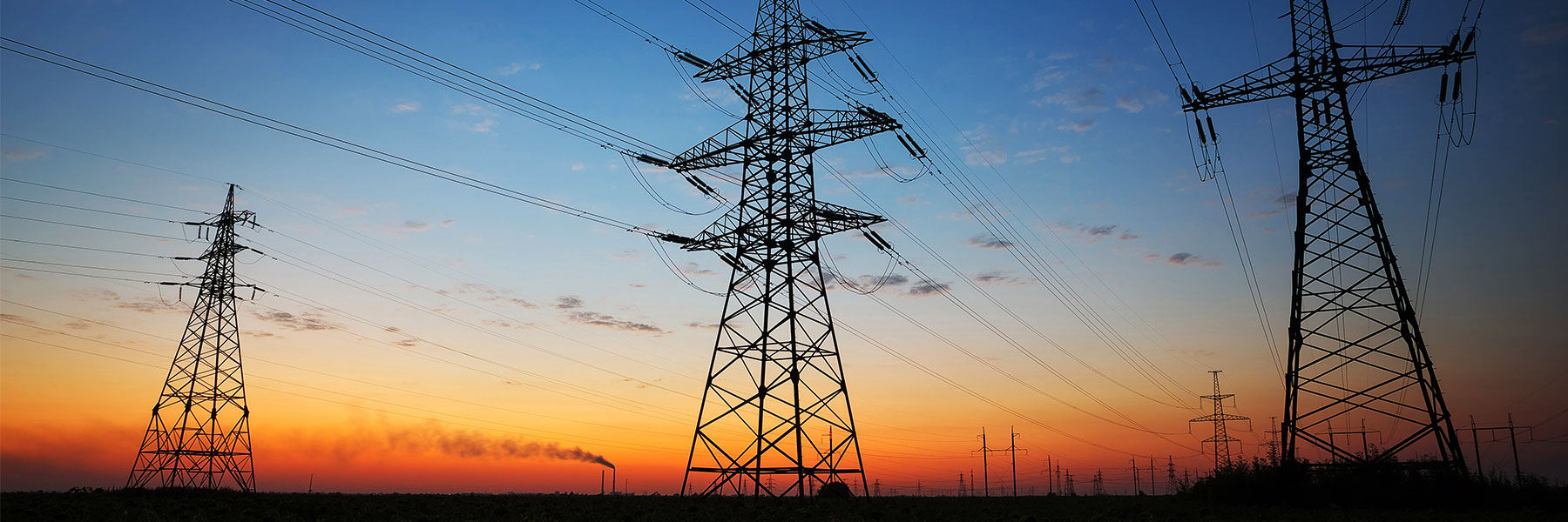 Silhouette of electricity pylons and high-voltage power lines on the field at sunset