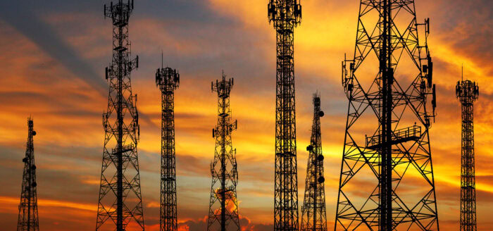 A group of communication towers are silhouetted against a vibrant sunset sky, showcasing their sleek design.